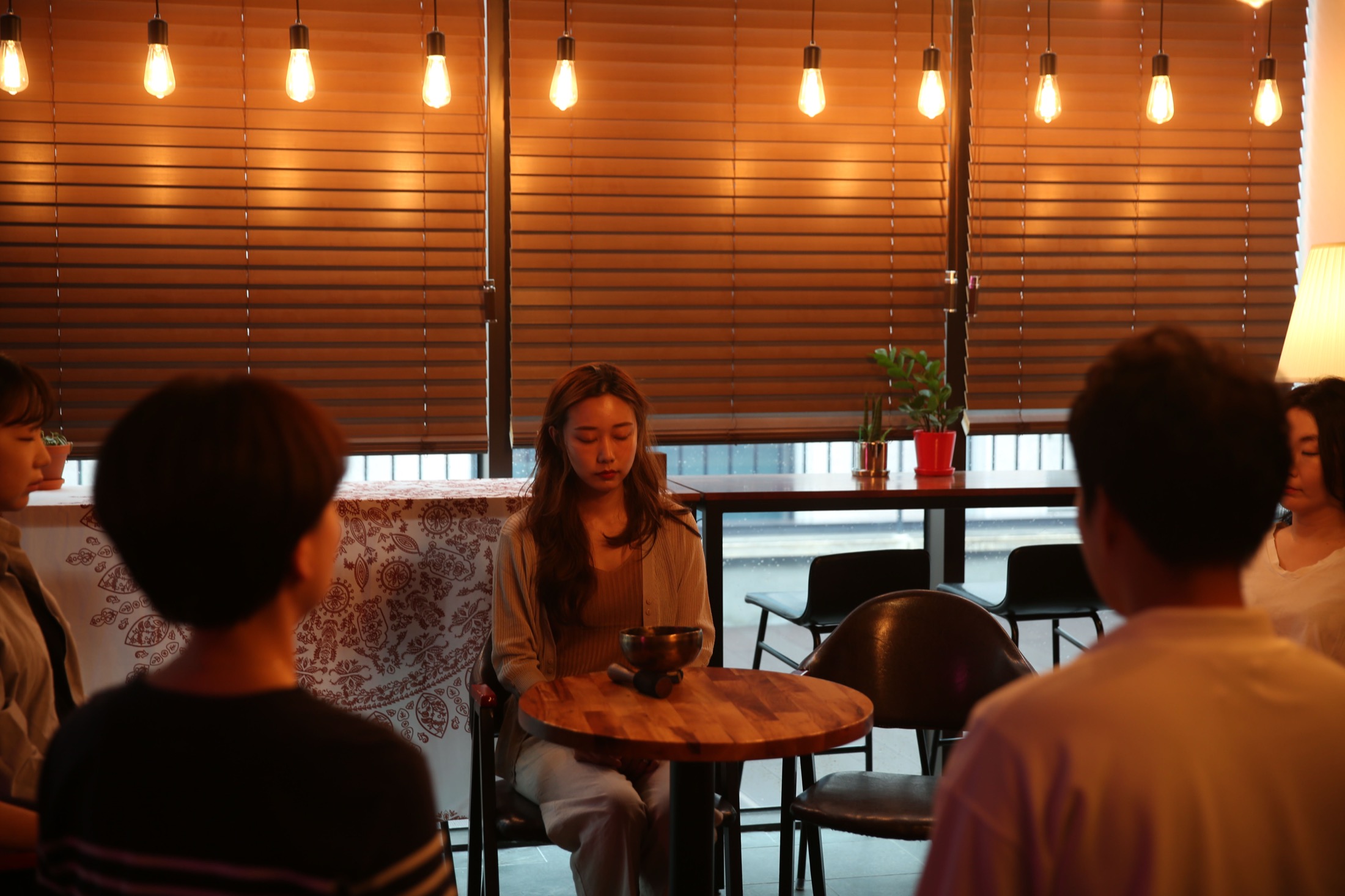 차분한 분위기의 명상 모임 풍경. 사람들이 둥글게 둘러앉아 눈을 감고 있다.